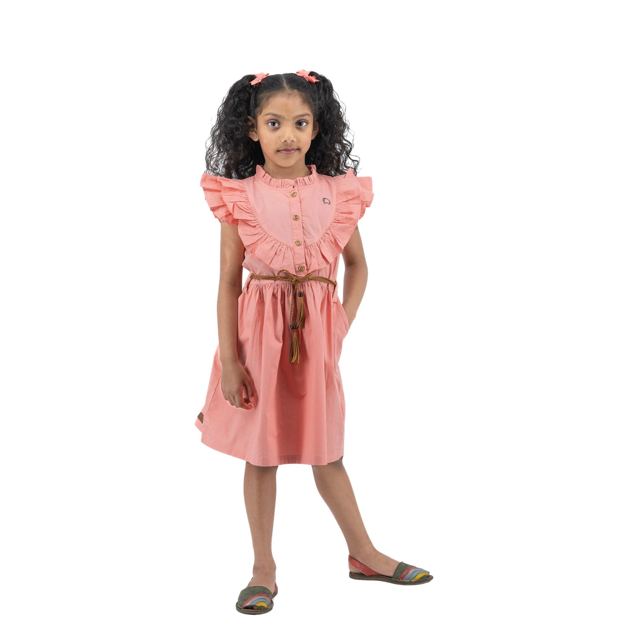 Young girl with curly hair, wearing a Karee Peach & Cream Butterfly Sleeve Cotton Dress and colorful sandals, standing on a white background.