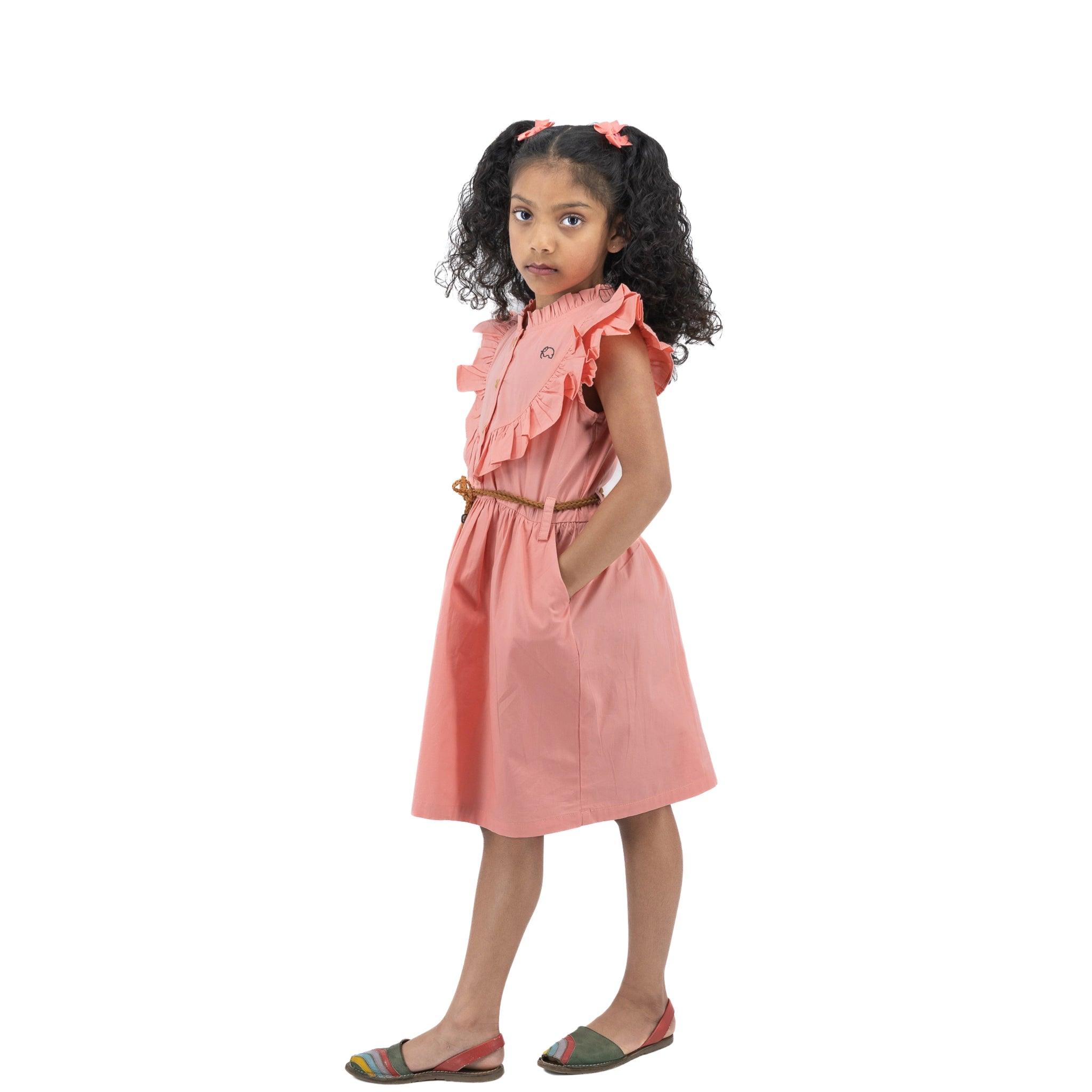 Young girl in a Karee Peach & Cream Butterfly Sleeve Cotton Dress with eco-friendly Karee wooden buttons, accessorized with a red hairband, standing against a white background, looking to the side with a thoughtful attitude.