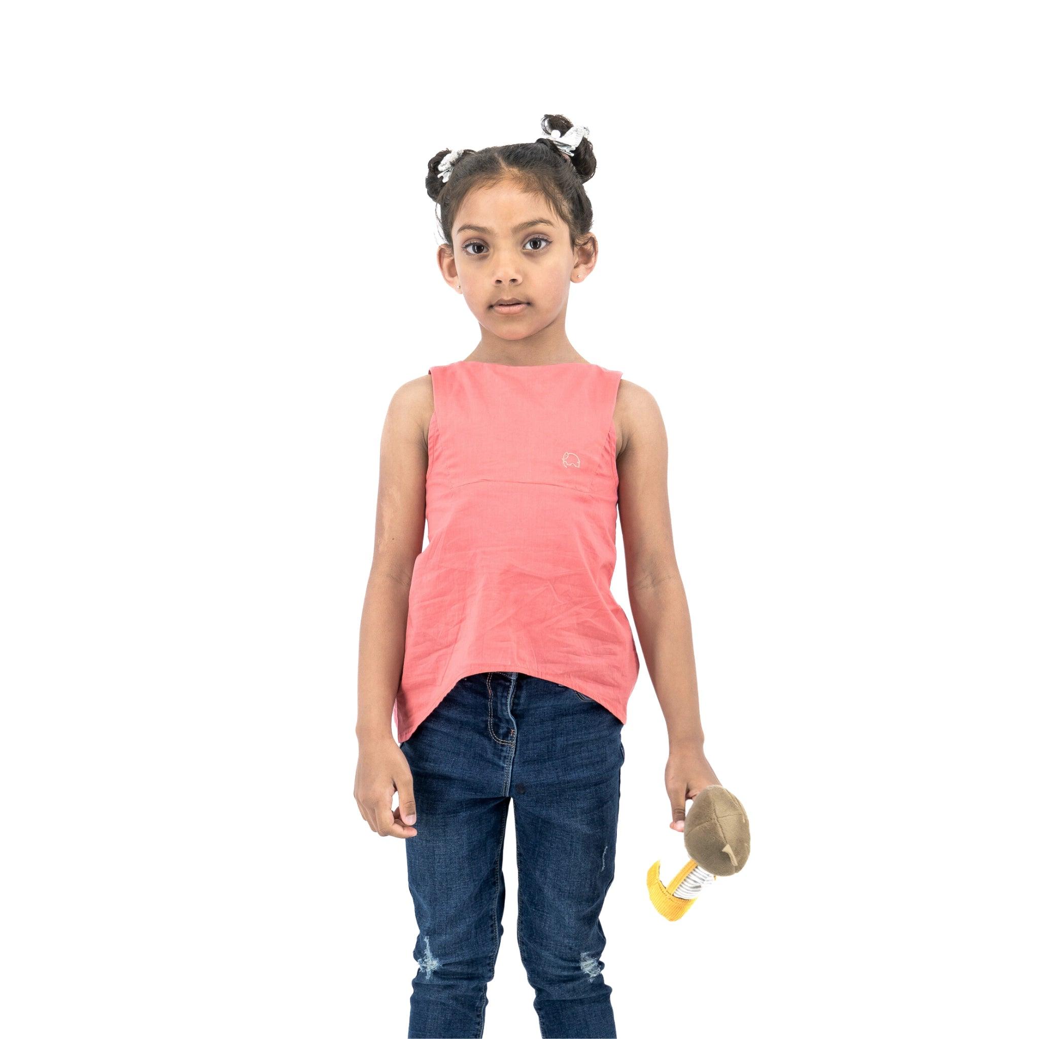 A young girl with buns in her hair, wearing a Karee Tea Rose Cotton Bib Neck Top for kids and jeans, holding a paintbrush, standing against a white background.