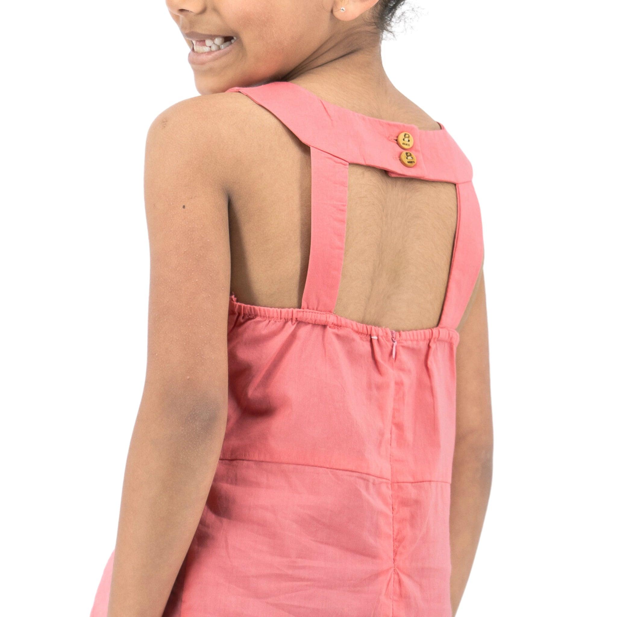 Young girl in a pink, Karee Tea Rose Cotton Bib Neck Top for kids turning her head to smile, viewed from behind against a white background.