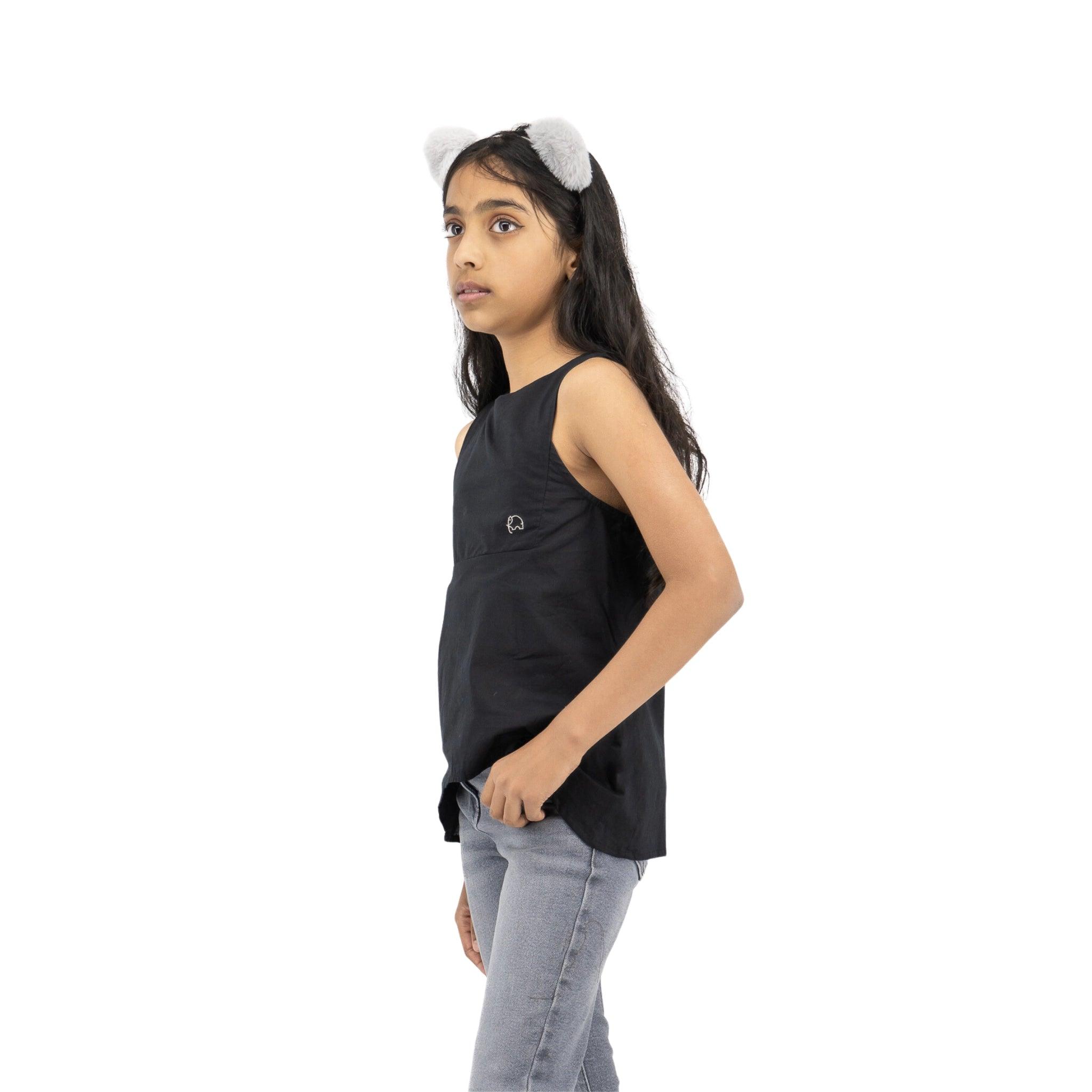 A girl in a Karee Black Beauty Cotton Bib Neck Top for kids and jeans, wearing cat ears, stands looking to the side against a white background.