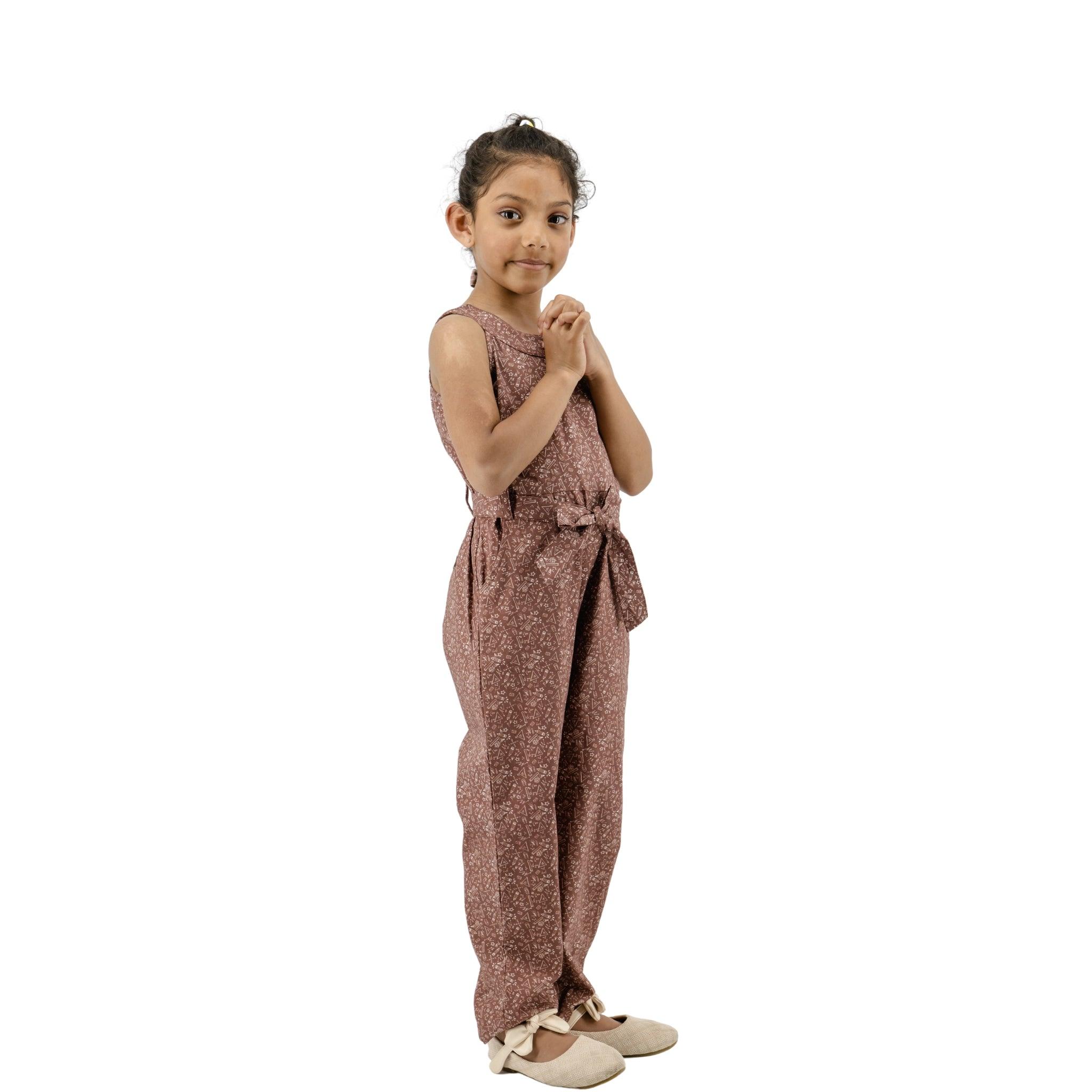 Young girl in a Karee cocoa brown cotton jumpsuit for girls posing with her hands together, standing against a white background.