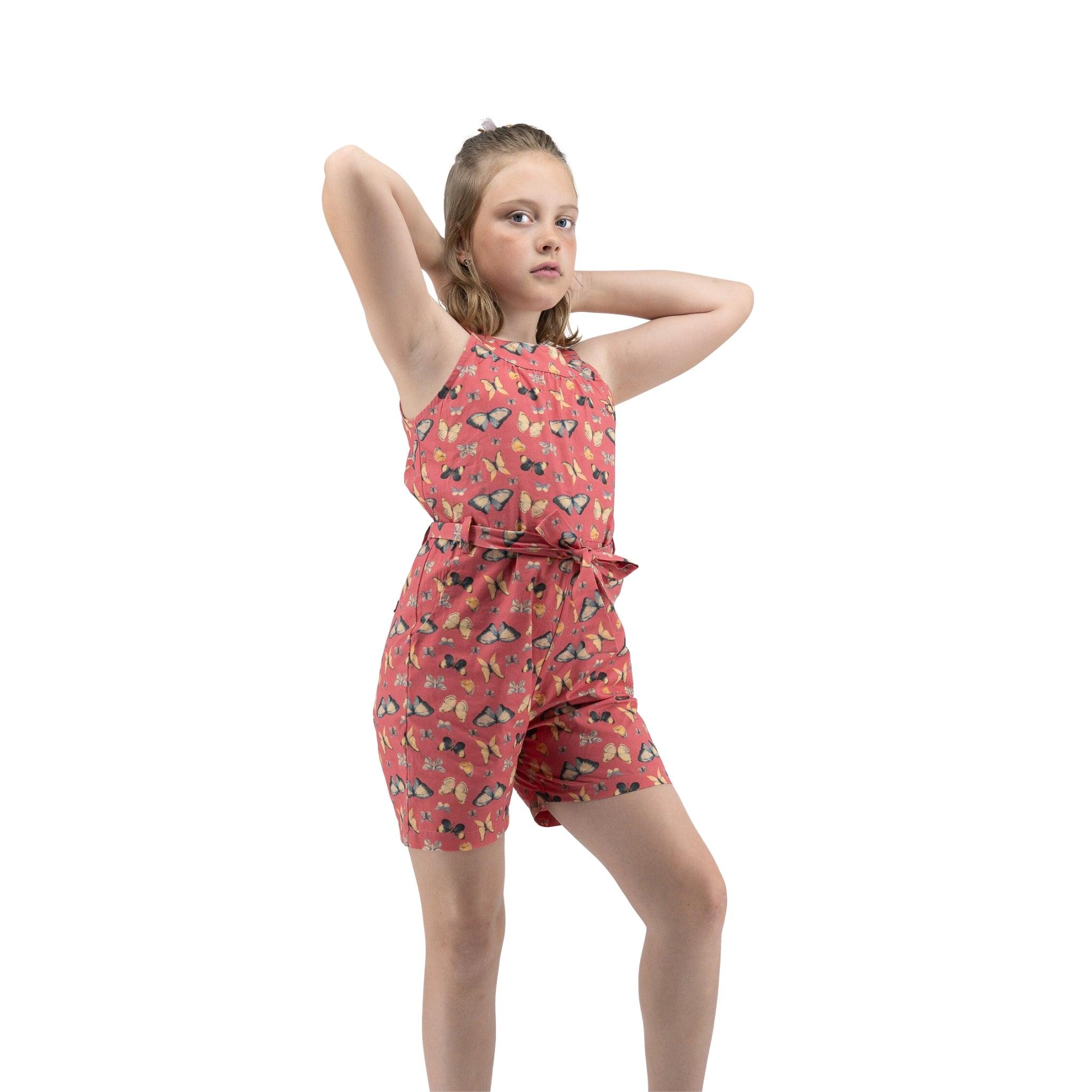 Young girl in a red floral Karee Ruby Trek Cotton Romper posing with one hand behind her head, isolated on a white background.