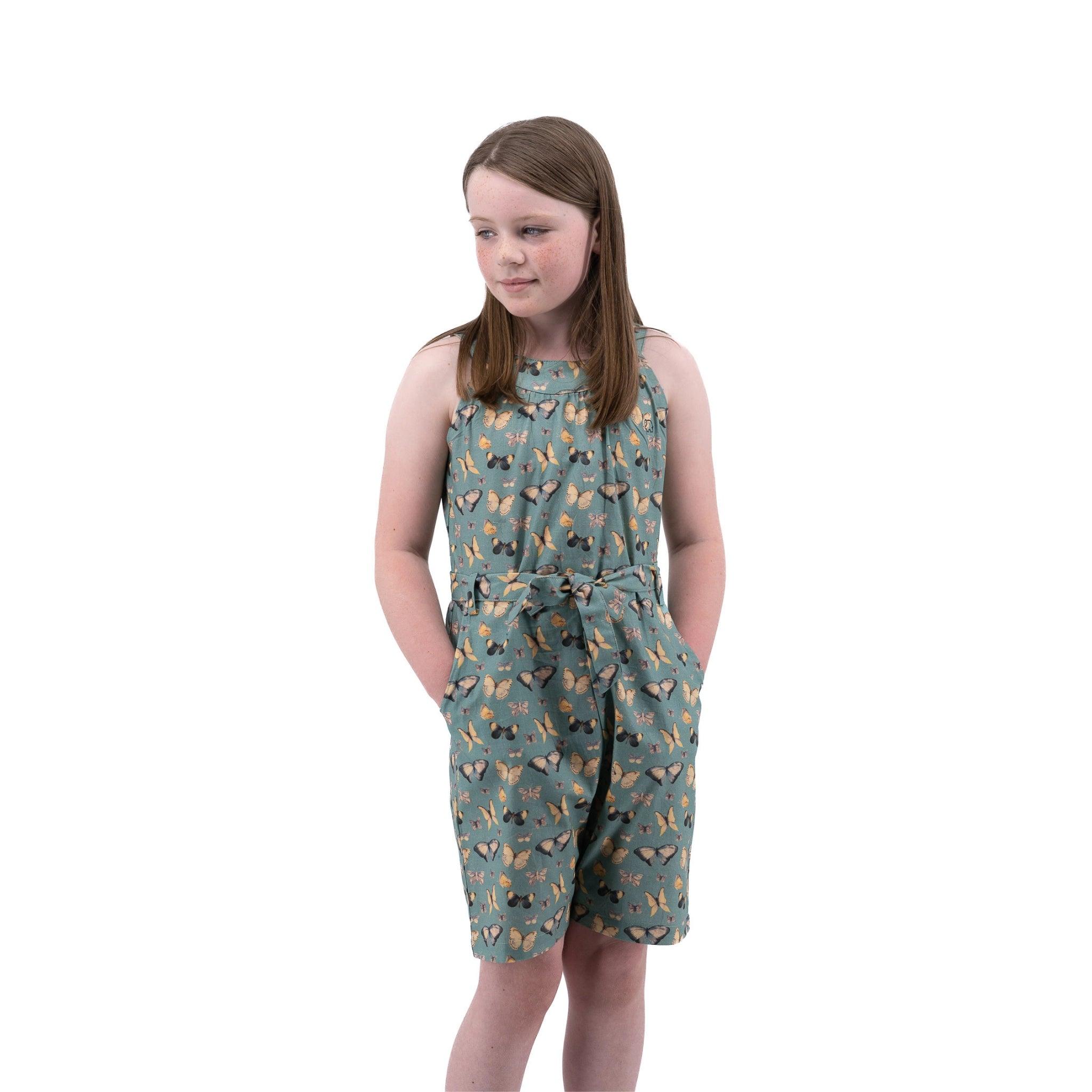 Young girl in a Karee Blue Surf Adventure-ready Cotton Play Suit standing against a white background, looking to her left with a thoughtful expression.