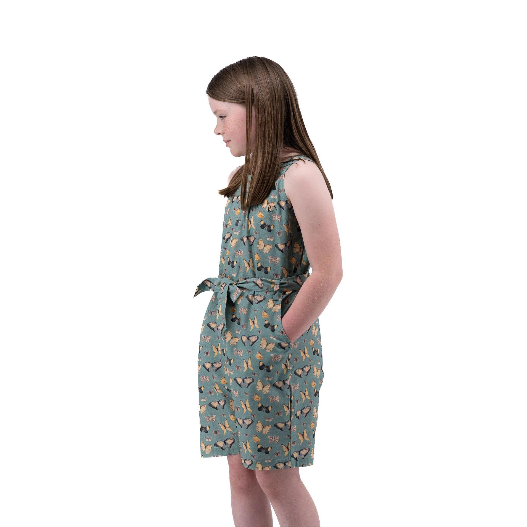 Young girl in a Karee Blue Surf Adventure-ready Cotton Play Suit standing sideways on a white background.