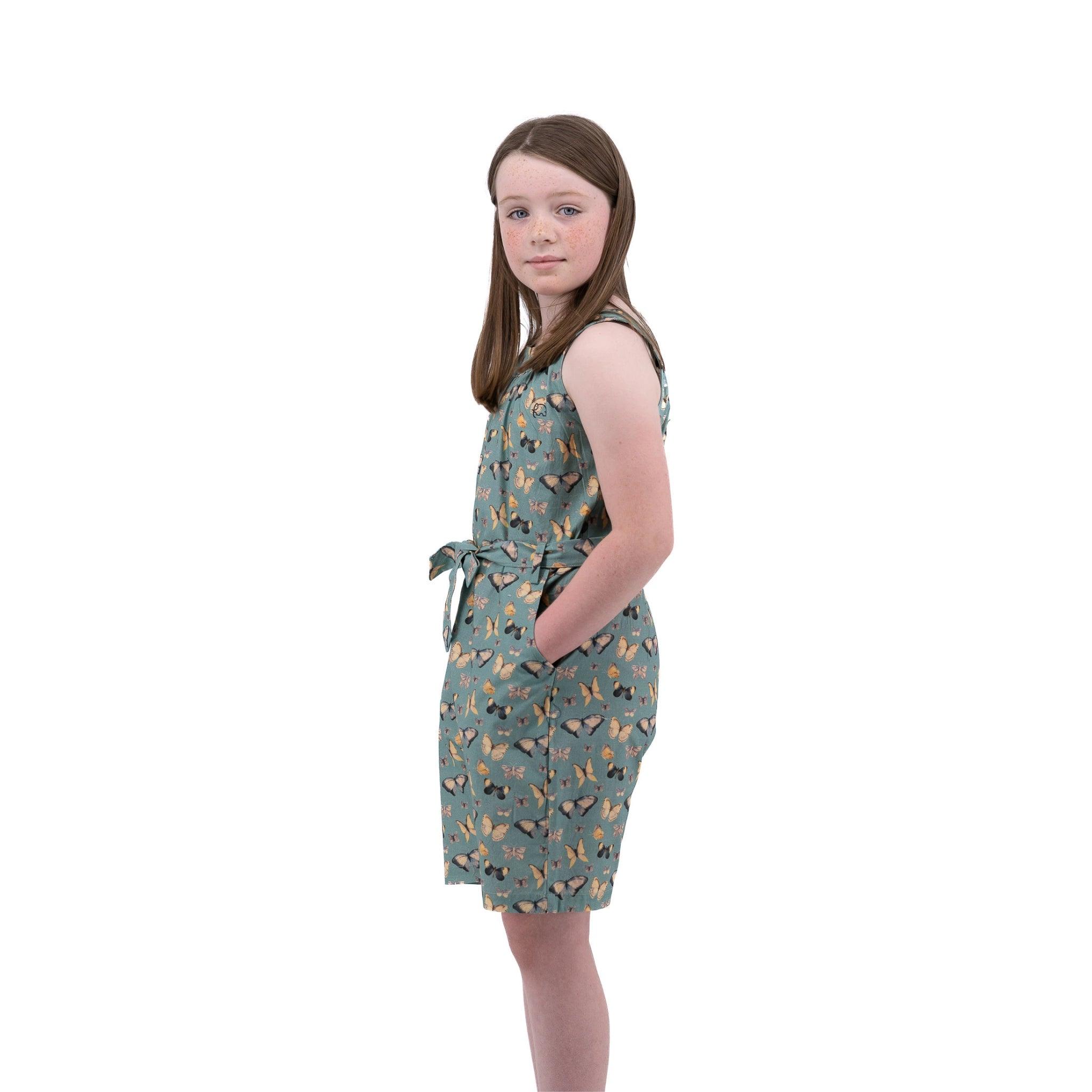 A young girl in a Karee Blue Surf Adventure-ready Cotton Play Suit with butterfly patterns stands against a white background, looking over her shoulder.