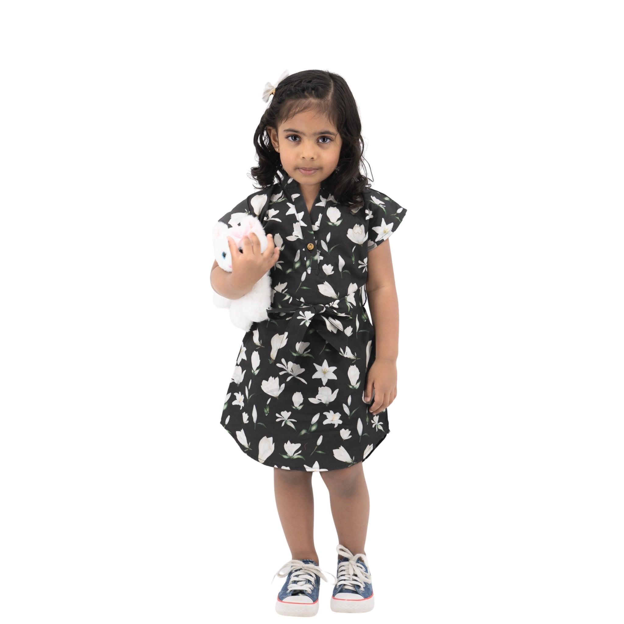Young girl in a Karee Black Lilly Blossom Cotton Shirt Dress holding a stuffed animal, standing against a white background.