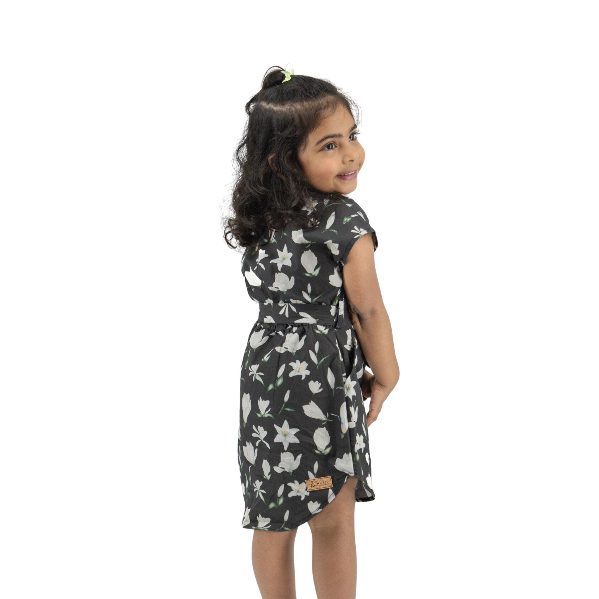 Young girl wearing a Karee Black Lilly Blossom Cotton Shirt Dress with a partial view, looking over her shoulder, isolated on a white background.