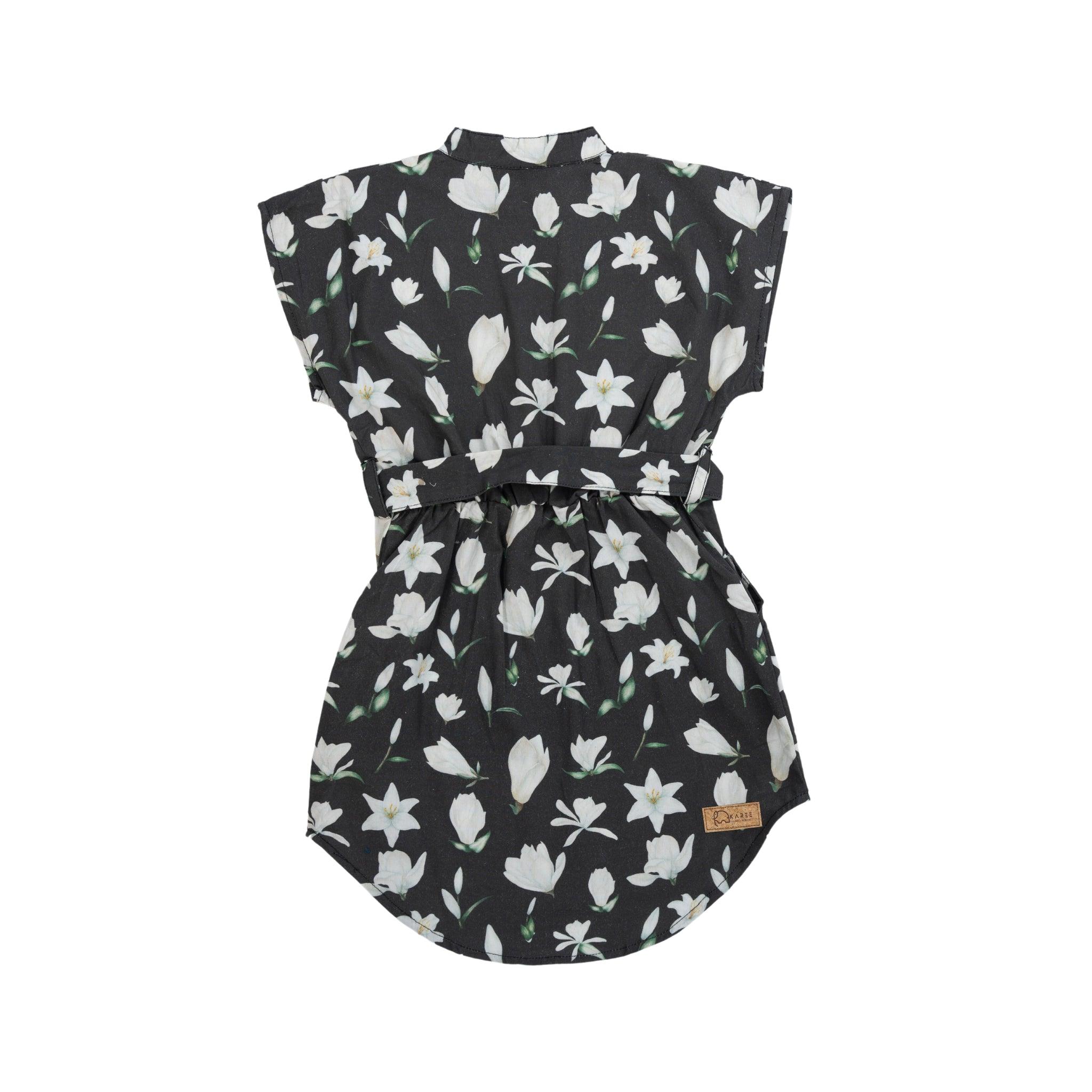 A sleeveless Black Lilly Blossom Cotton Shirt Dress with a white floral pattern, cinched at the waist with a tie, crafted in eco-friendly poplin cotton, displayed against a white background by Karee.