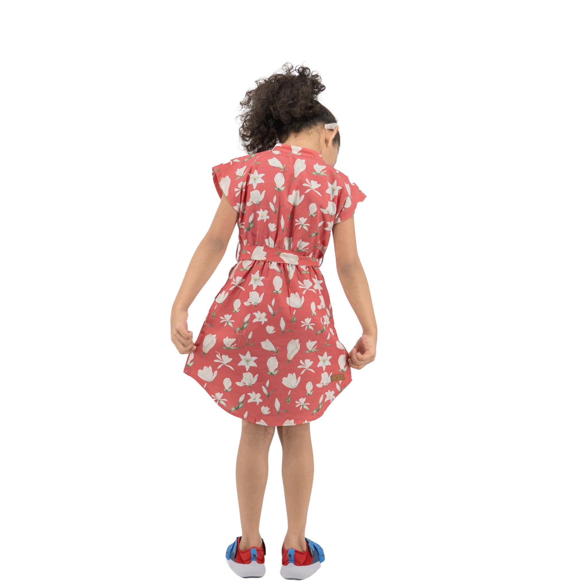 Young girl with curly hair, seen from behind, wearing a premium cotton Karee Mineral Red Lilly Blossom Cotton Shirt Dress and blue shoes, standing against a white background.