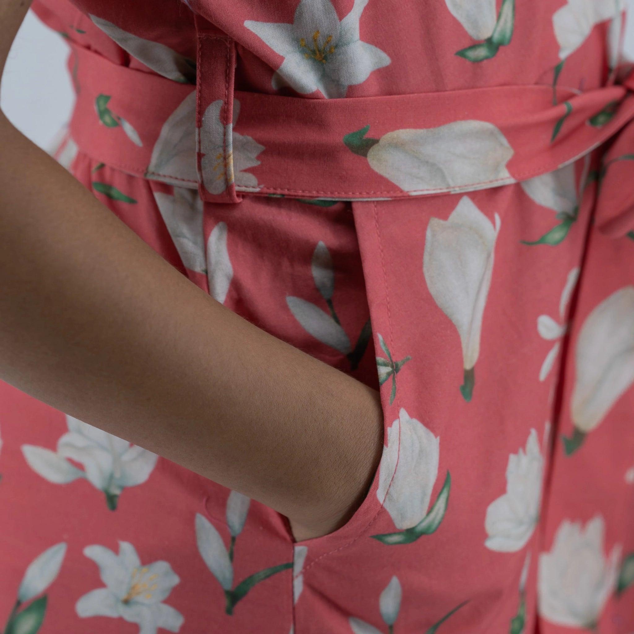 Close-up of a person wearing a pink floral "Karee Mineral Red Lilly Blossom Cotton Shirt Dress" with a focus on the fabric texture and belt detail.