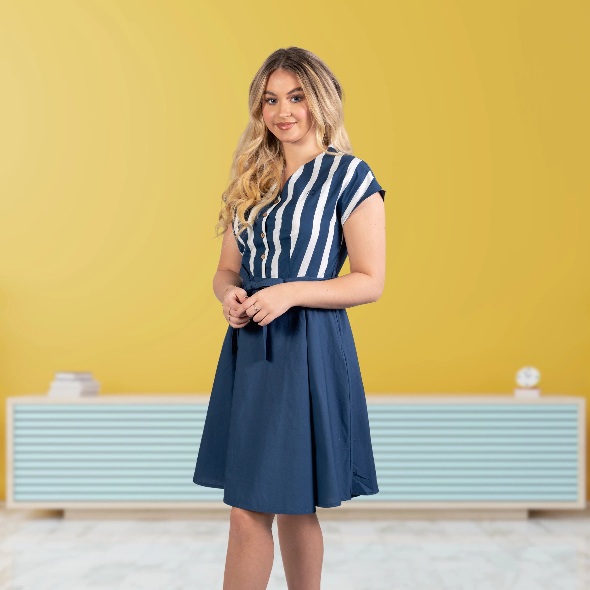 A woman wearing a beautiful Karee Blue and white stripe dress, in a studio 