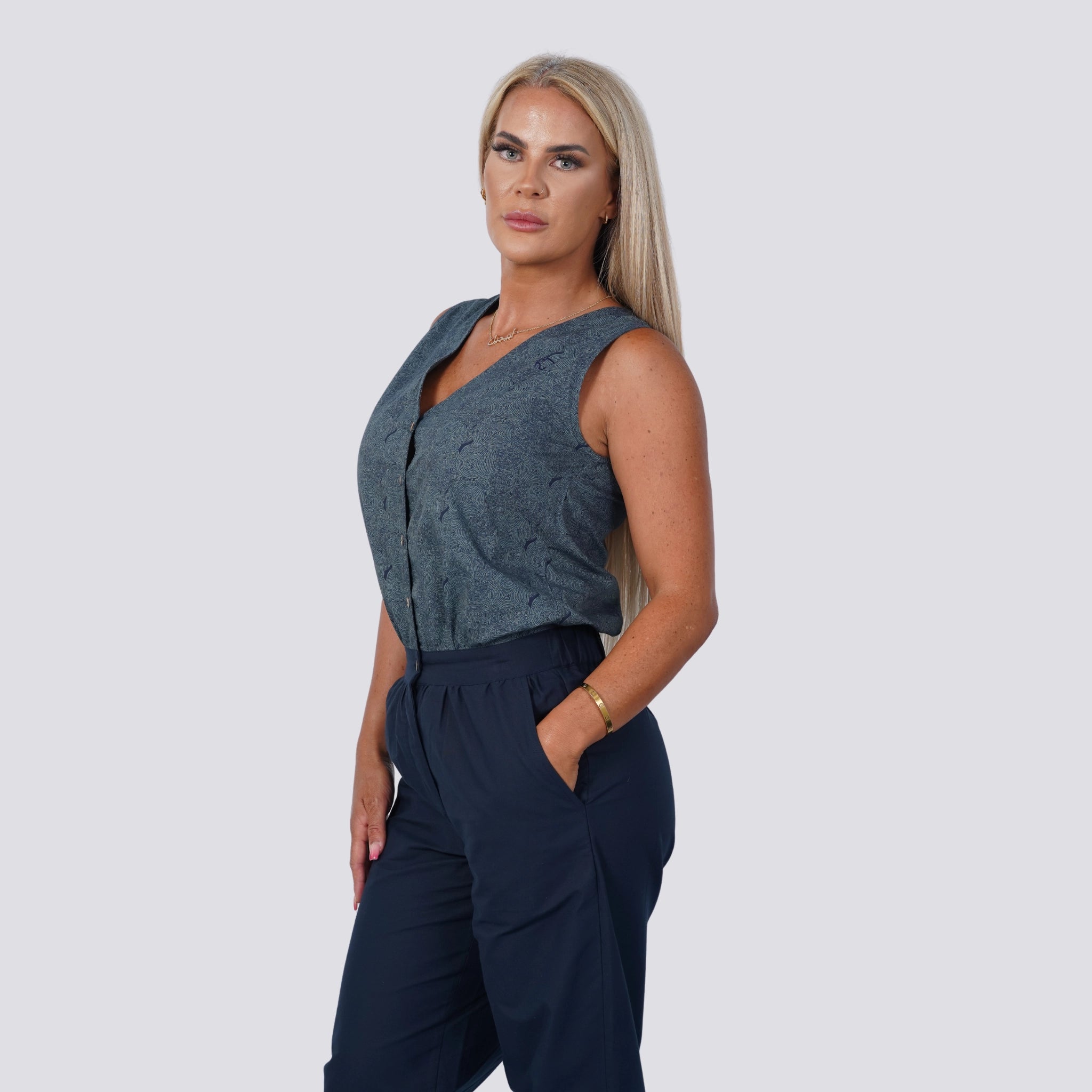 A person with long blond hair wearing the Embrace Coastal Chic with Sustainability: Navy Nights Golden Palm Leaves Linen Shirt Dress from Karee stands with one hand in their pocket against a plain background.