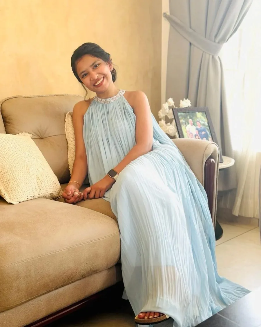 Sara V Regi, founder and designer of Seasons by Sarah, smiling on a sofa in a pale blue pleated halter gown