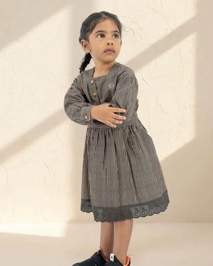 A girl in the Black stripe long puff-sleeve cotton dress with a broderie anglaise hem, arms folded