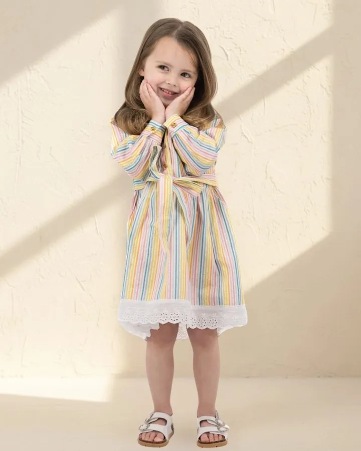 Girls' autumn dress: a smiling girl in the Rainbow stripe long puff-sleeve cotton dress with a white broderie hem